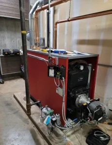A red industrial boiler unit with exposed electrical wiring and copper piping in a mechanical utility room.